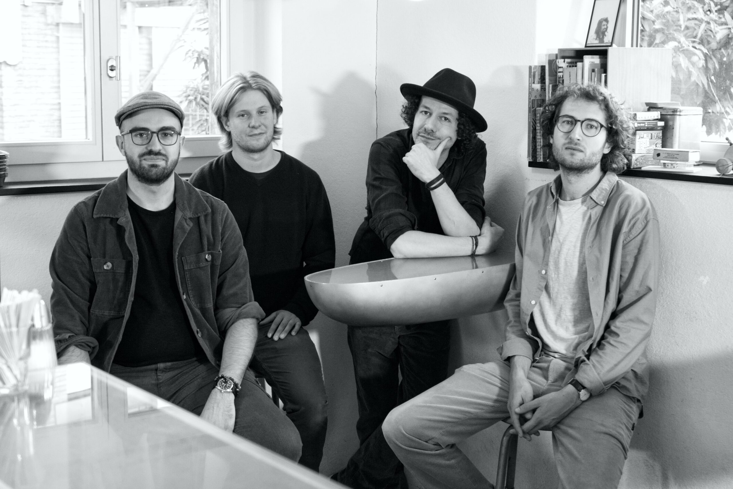Schwarz-weiss-Foto: Die Mitglieder der Band Kühnrad Lohse sitzen und stehen um einen Tisch in der Bar Portier in Winterthur.
