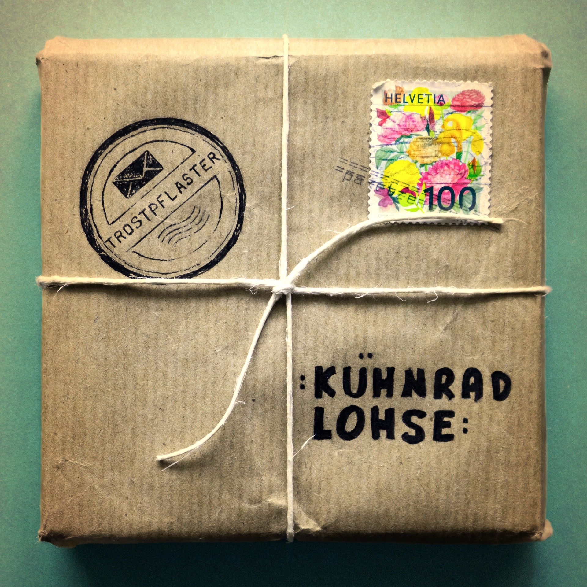 Cover Kühnrad Lohse Trostpflaster Cover des Albums «Trostpflaster»: Ein in Packpapier und mit Schnur eingewickeltes Paket vor türkisem Hintergrund, auf dem Packpapier eine Briefmarke sowie je ein Stempel «Trostpflaster» und «Kühnrad Lohse».